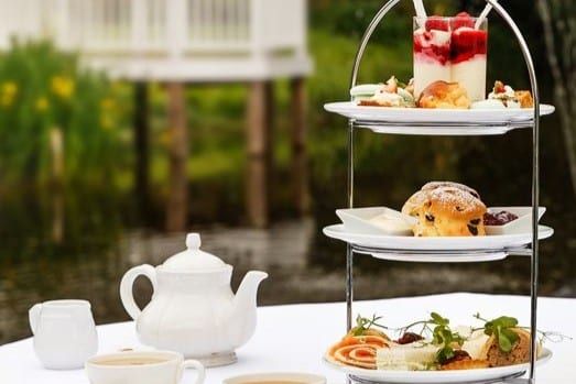 A three tier afternoon tea stand with a teapot, set beside the millpond and gazebo at Sheene Mill