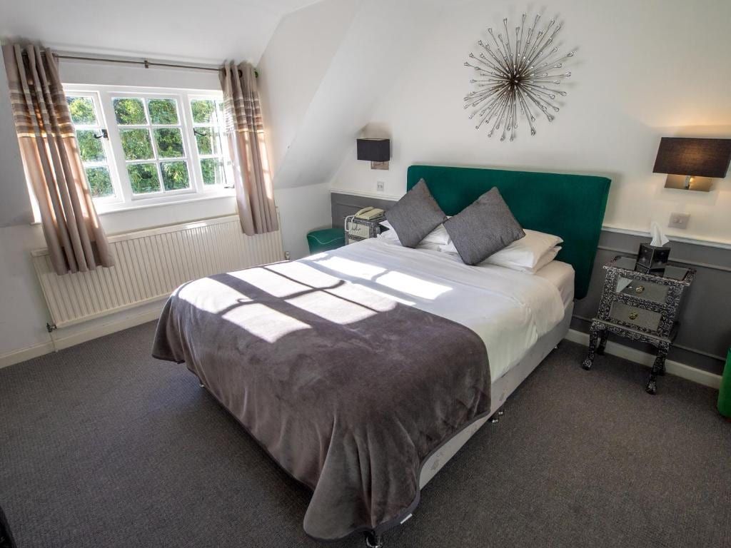 A boutique bedroom at Sheene Mill with a green velvet headboard, eaves window and individually designed interiors, Melbourn, Cambridgeshire