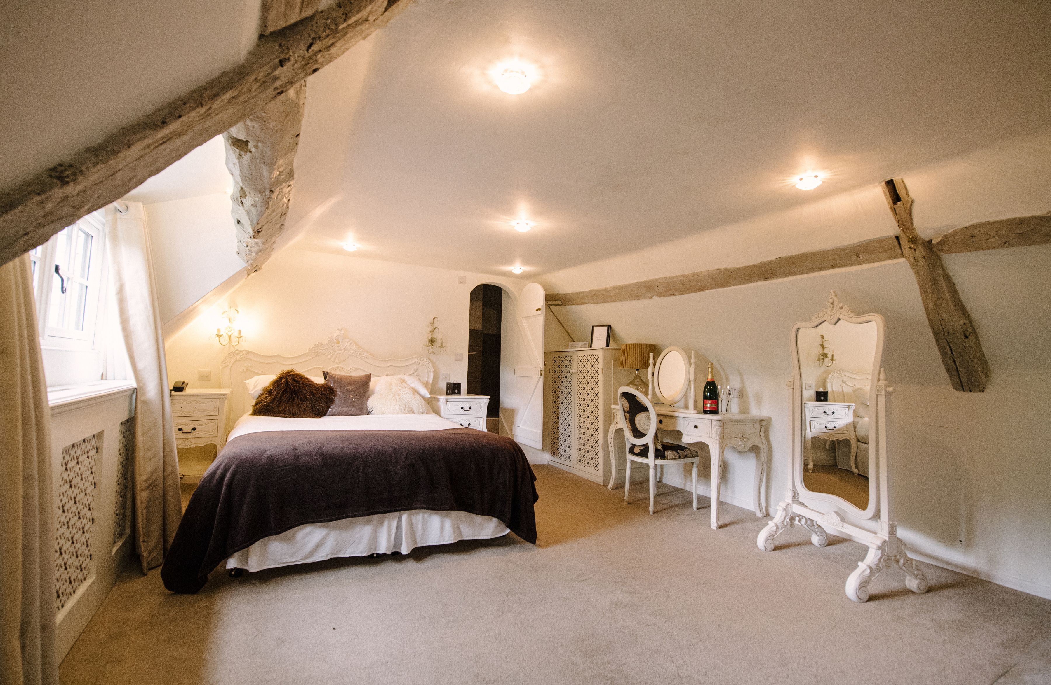 A boutique en-suite bedroom under the eaves at Sheene Mill, with original beams and a dressing table, Melbourn, Cambridgeshire