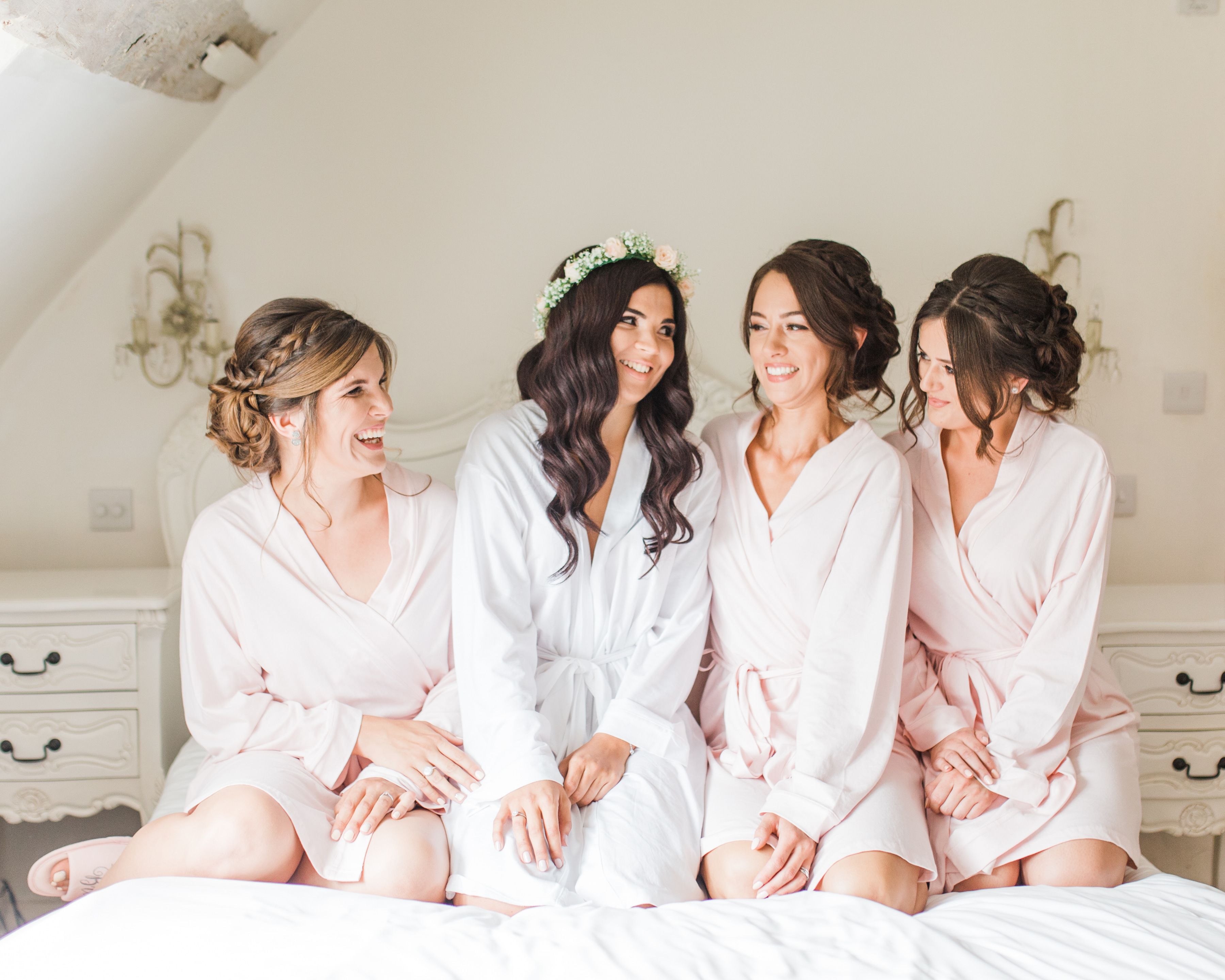 A bride and her bridesmaids in matching robes laughing together while getting ready at Sheene Mill