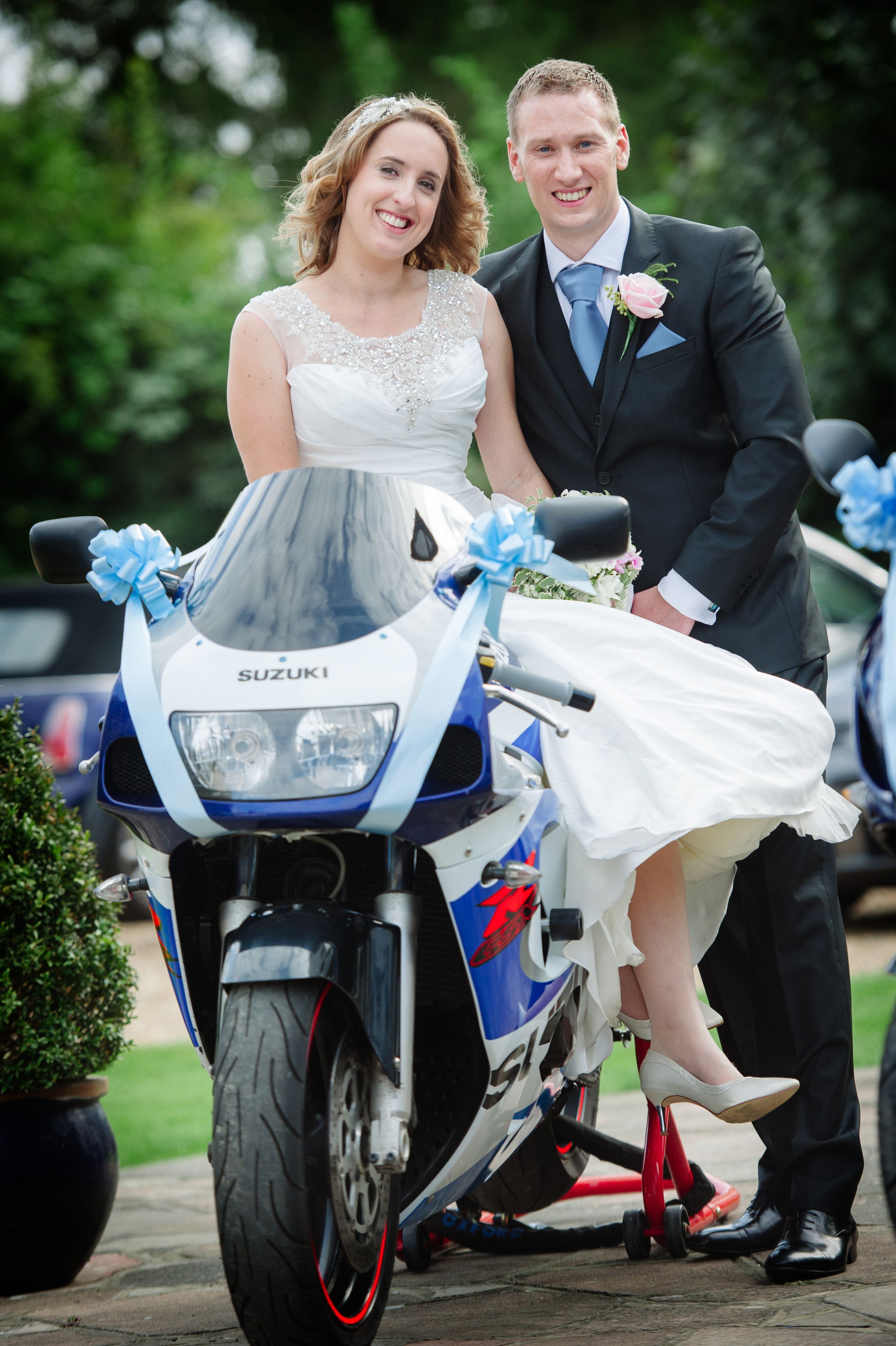A bride perched on a ribbon dressed motorbike beside her groom at Sheene Mill