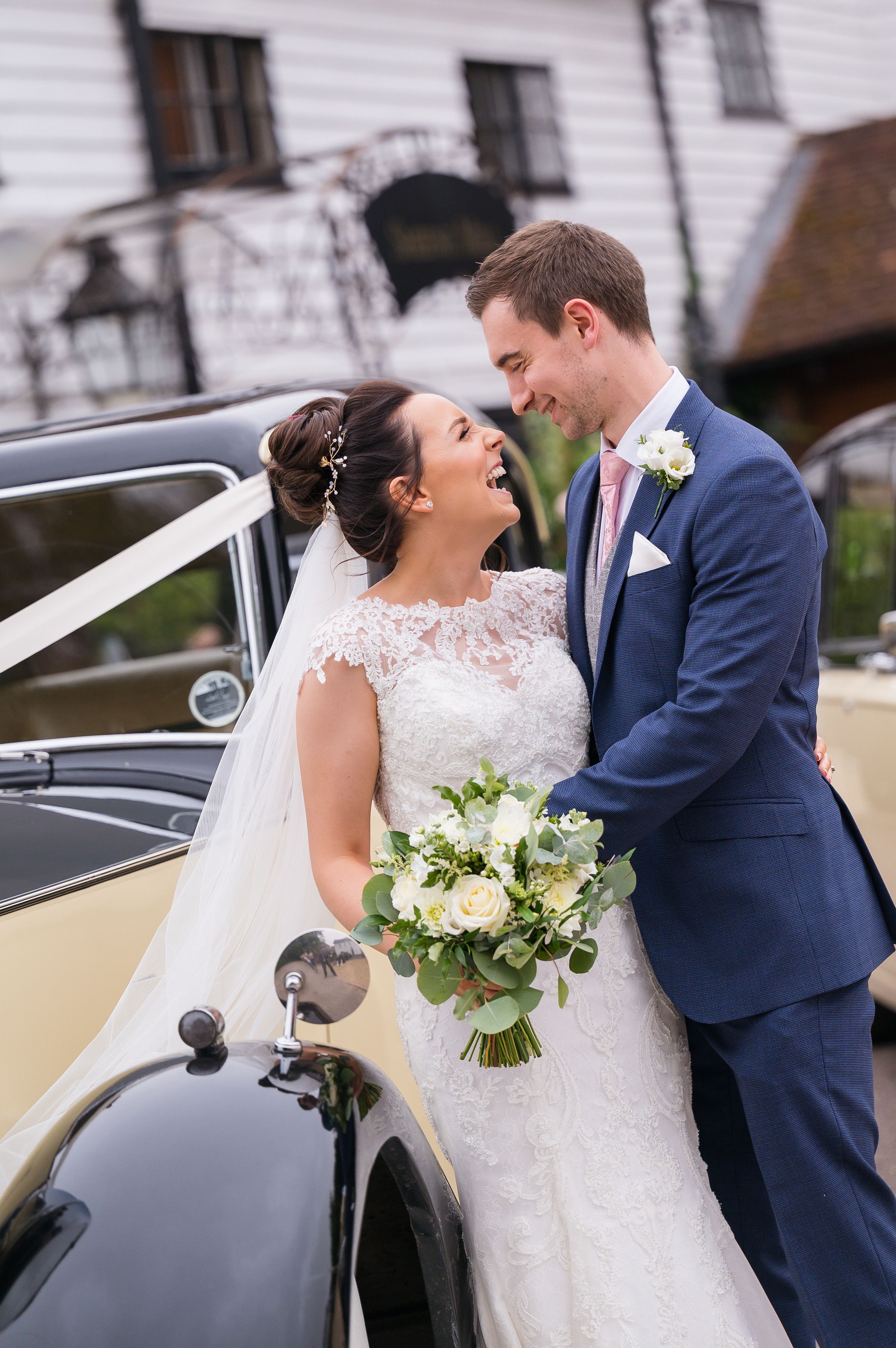 A bride and groom sharing a smile beside a vintage wedding car at Sheene Mill