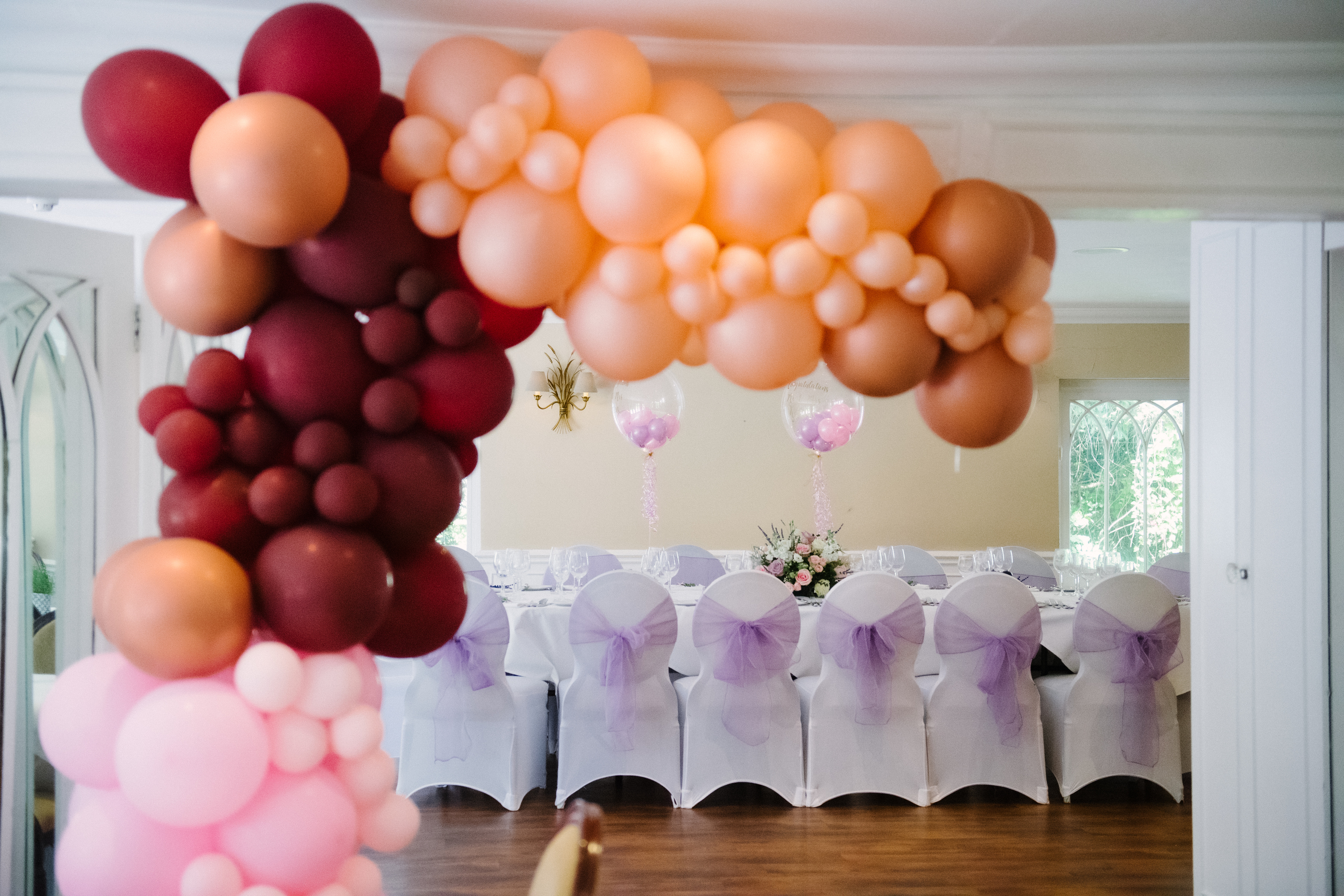 A burgundy and blush balloon arch over a room dressed for a celebration at Sheene Mill