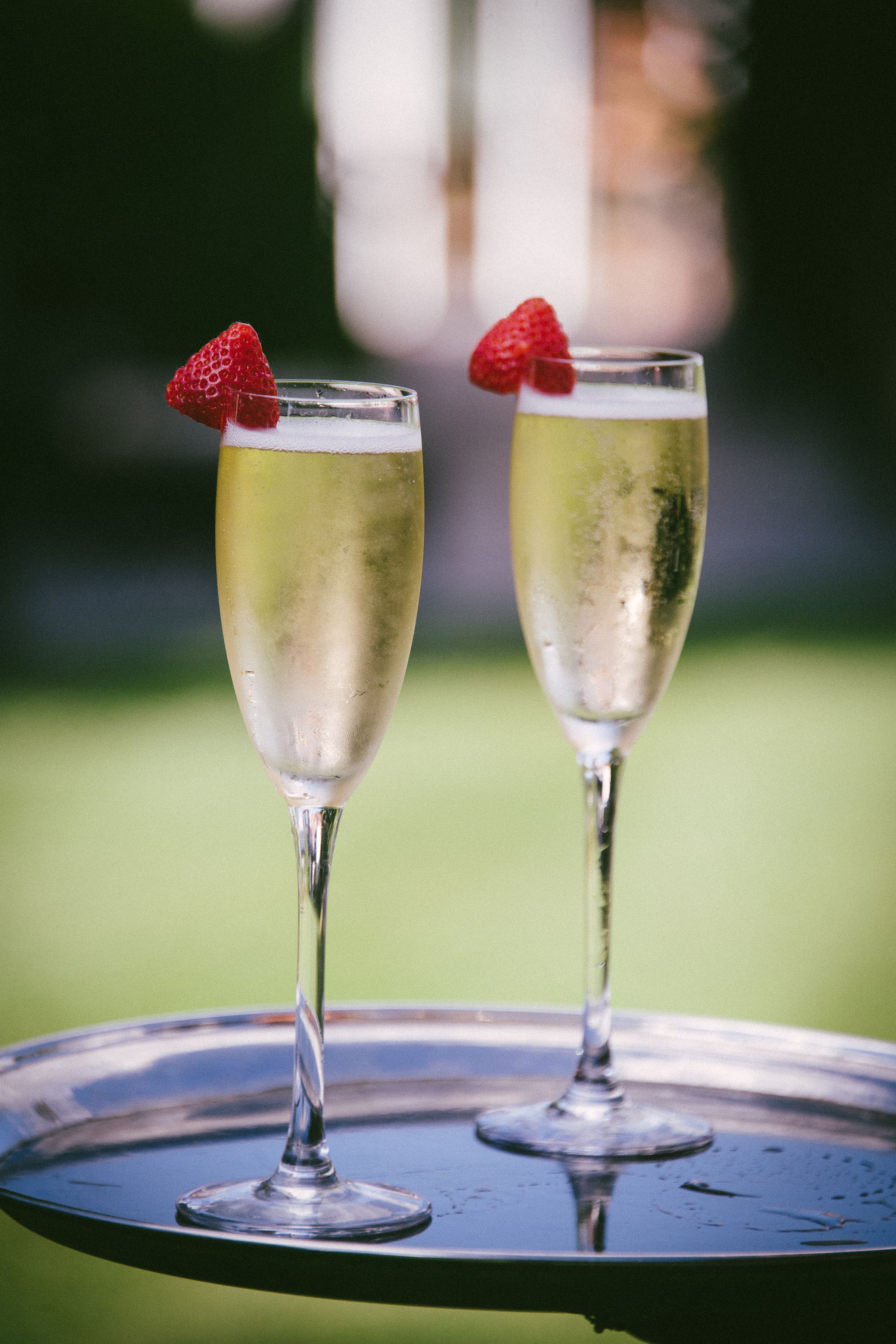 Two flutes of champagne topped with strawberries on a silver tray in the gardens at Sheene Mill