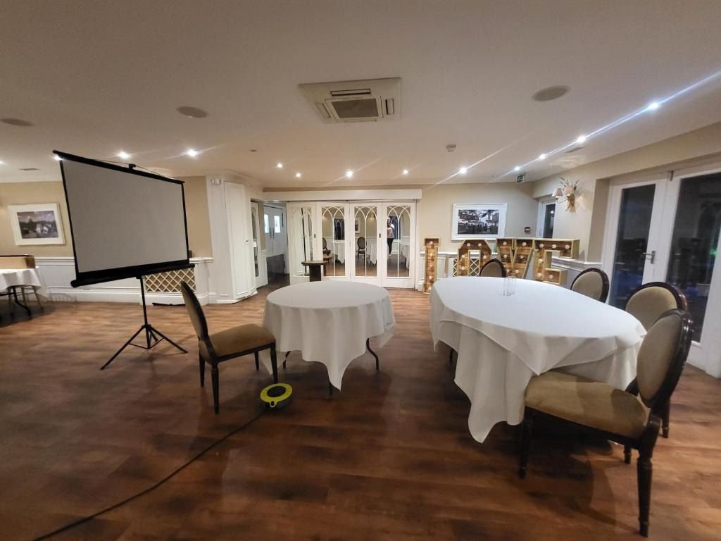 A meeting room at Sheene Mill set up for a corporate event with a projector screen and round delegate tables, Melbourn, Cambridgeshire