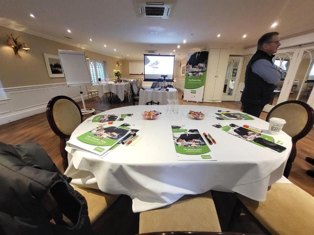 A meeting room at Sheene Mill set up for a corporate training day, with a round table of delegate materials, a projector screen and a flip chart, Melbourn, Cambridgeshire