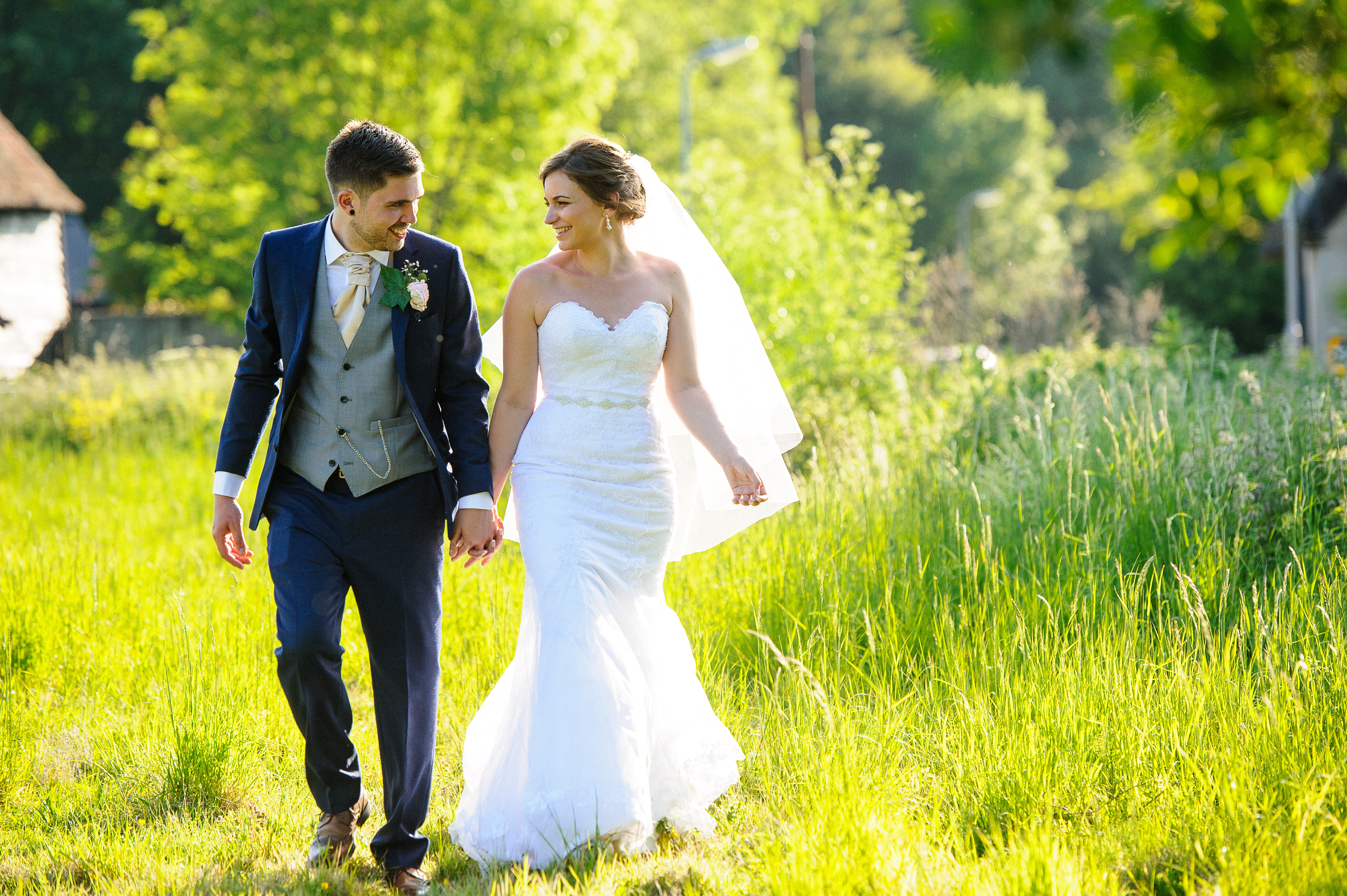 A newly married couple walking hand in hand through the long summer grass at Sheene Mill, Melbourn, Cambridgeshire