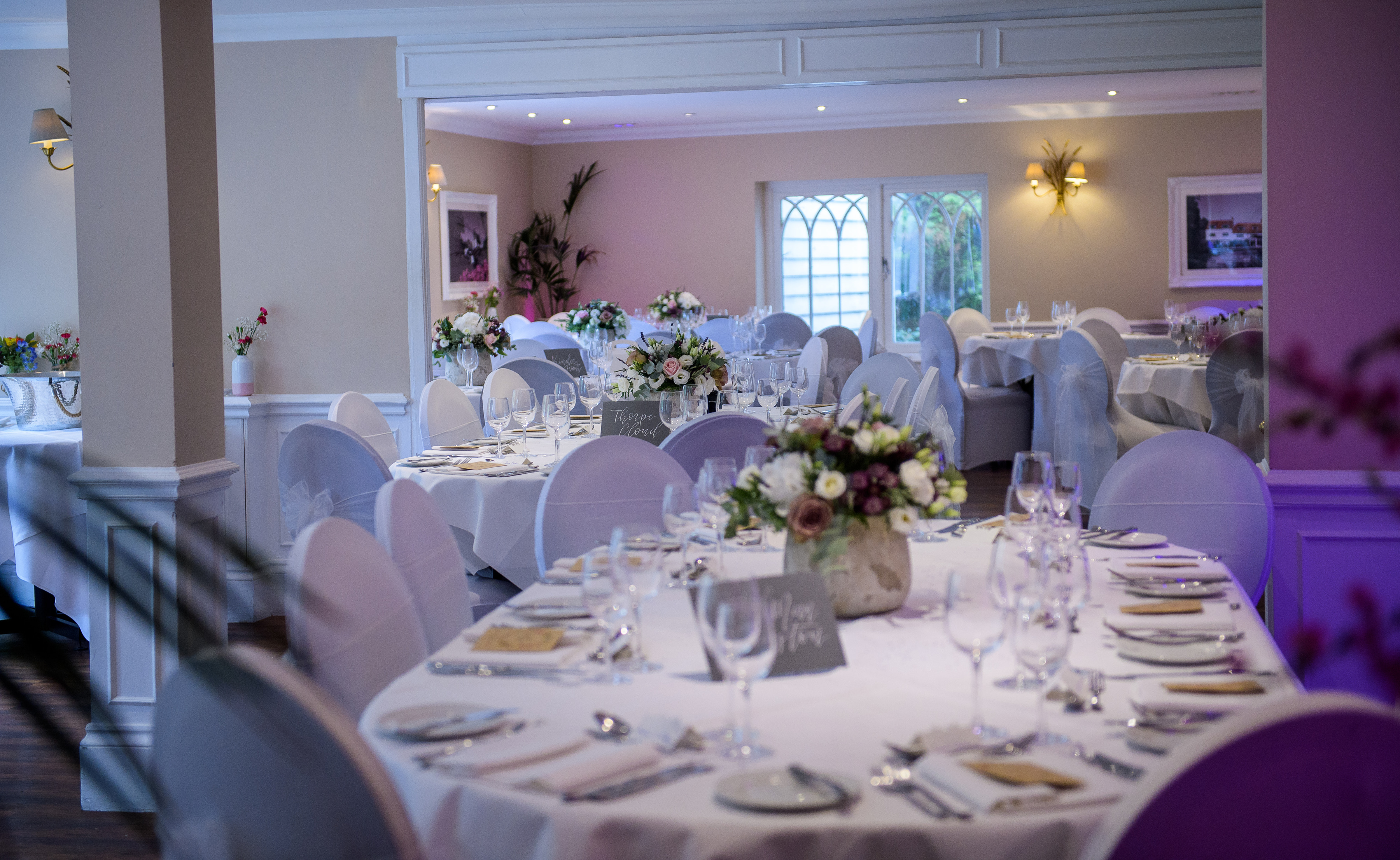 Round tables laid with white linen, glassware and seasonal flowers in the dining room at Sheene Mill, a sixteenth century mill venue in Melbourn, Cambridgeshire