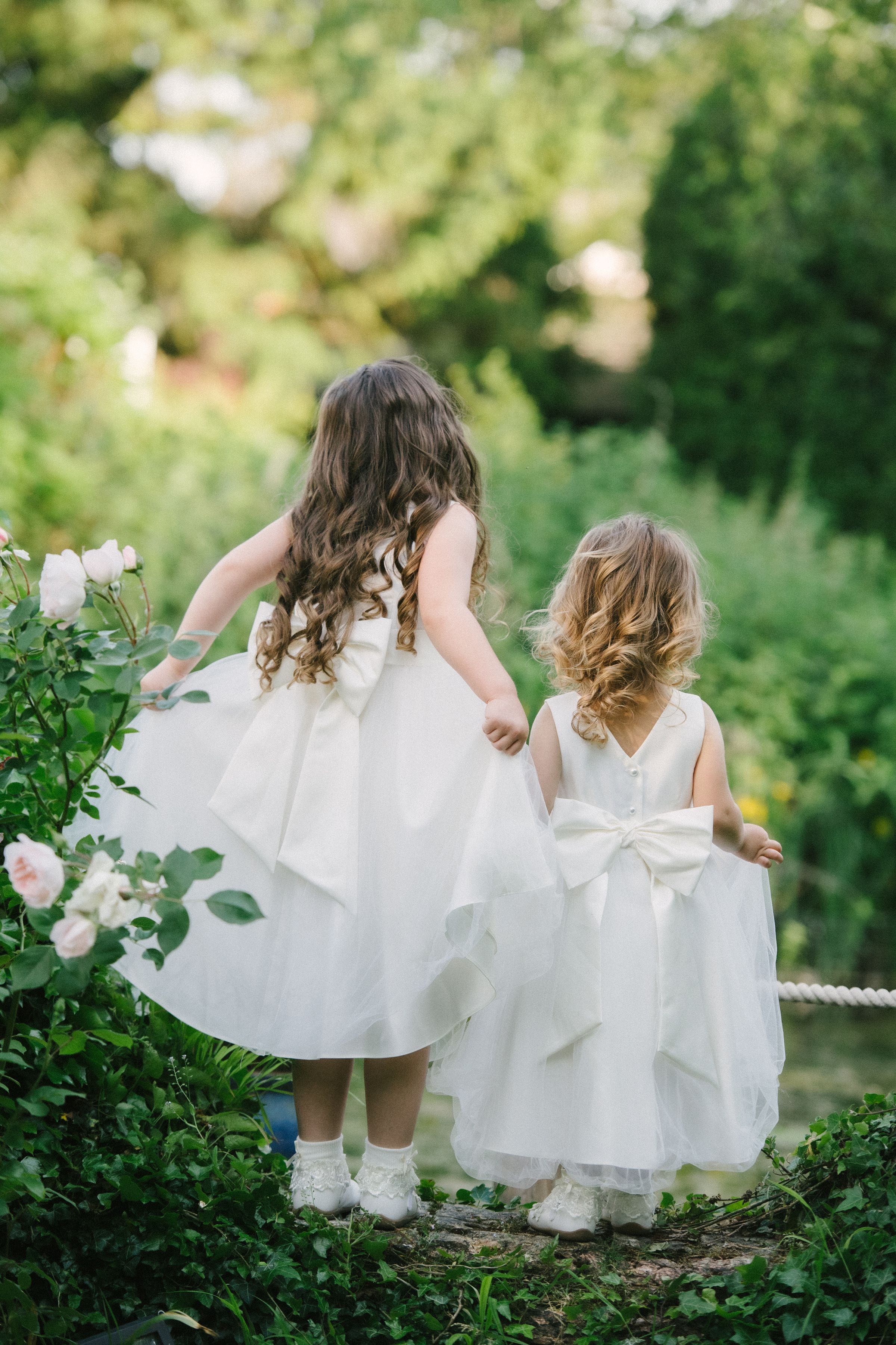 Two flower girls in white dresses walking among roses in the gardens at Sheene Mill