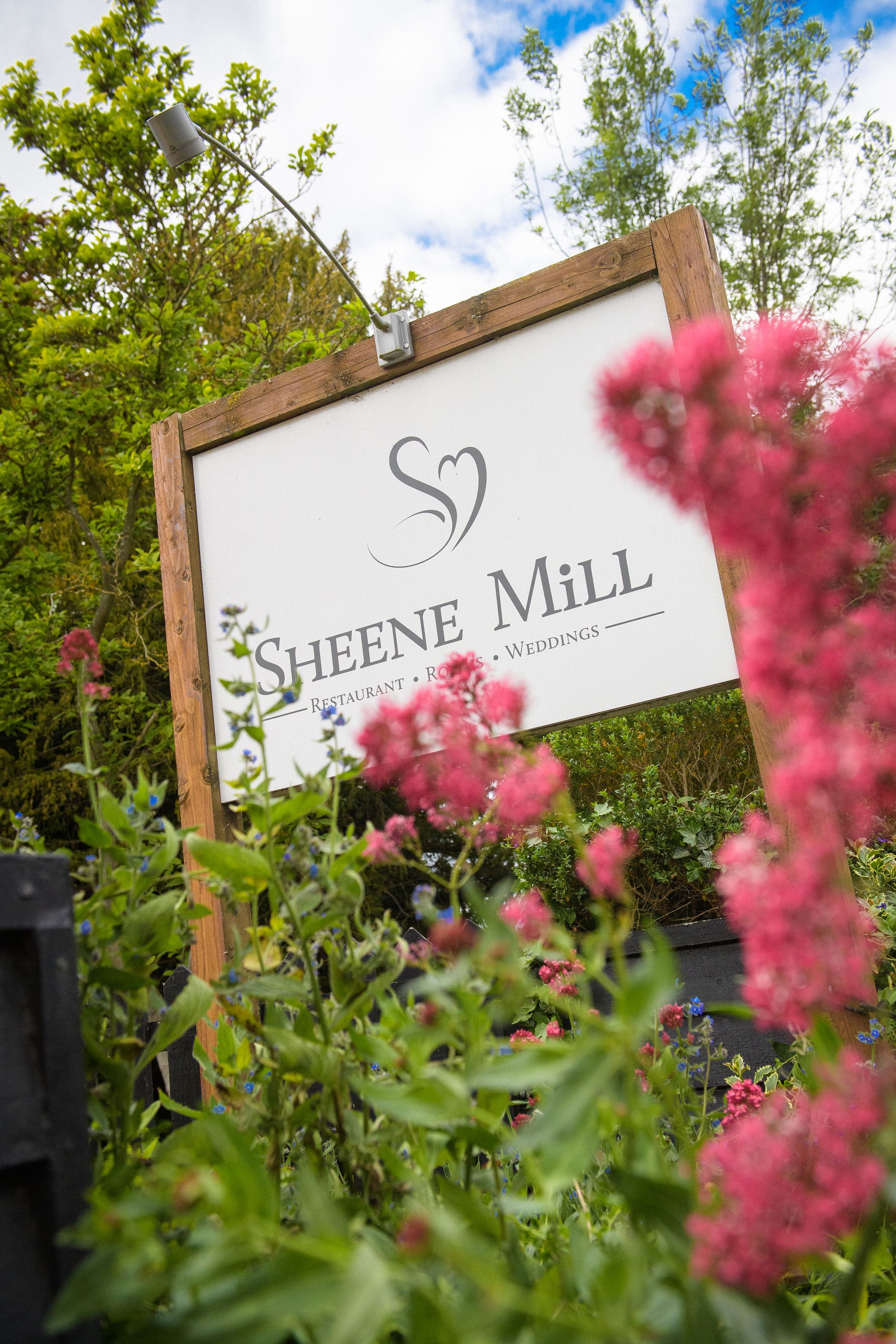 The Sheene Mill sign framed by pink flowers in the gardens