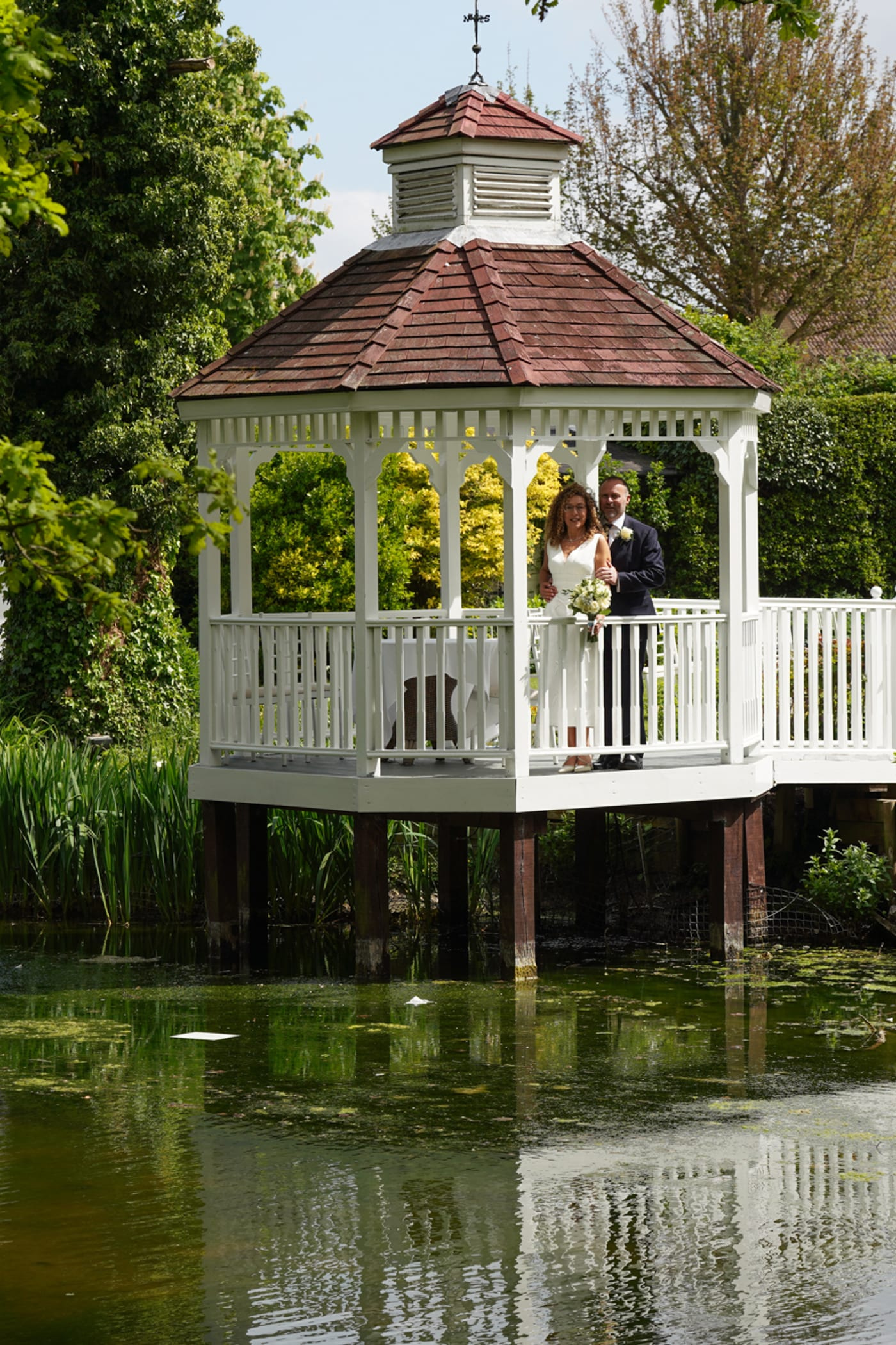 A couple on the white gazebo seen across the millpond at Sheene Mill in Cambridgeshire