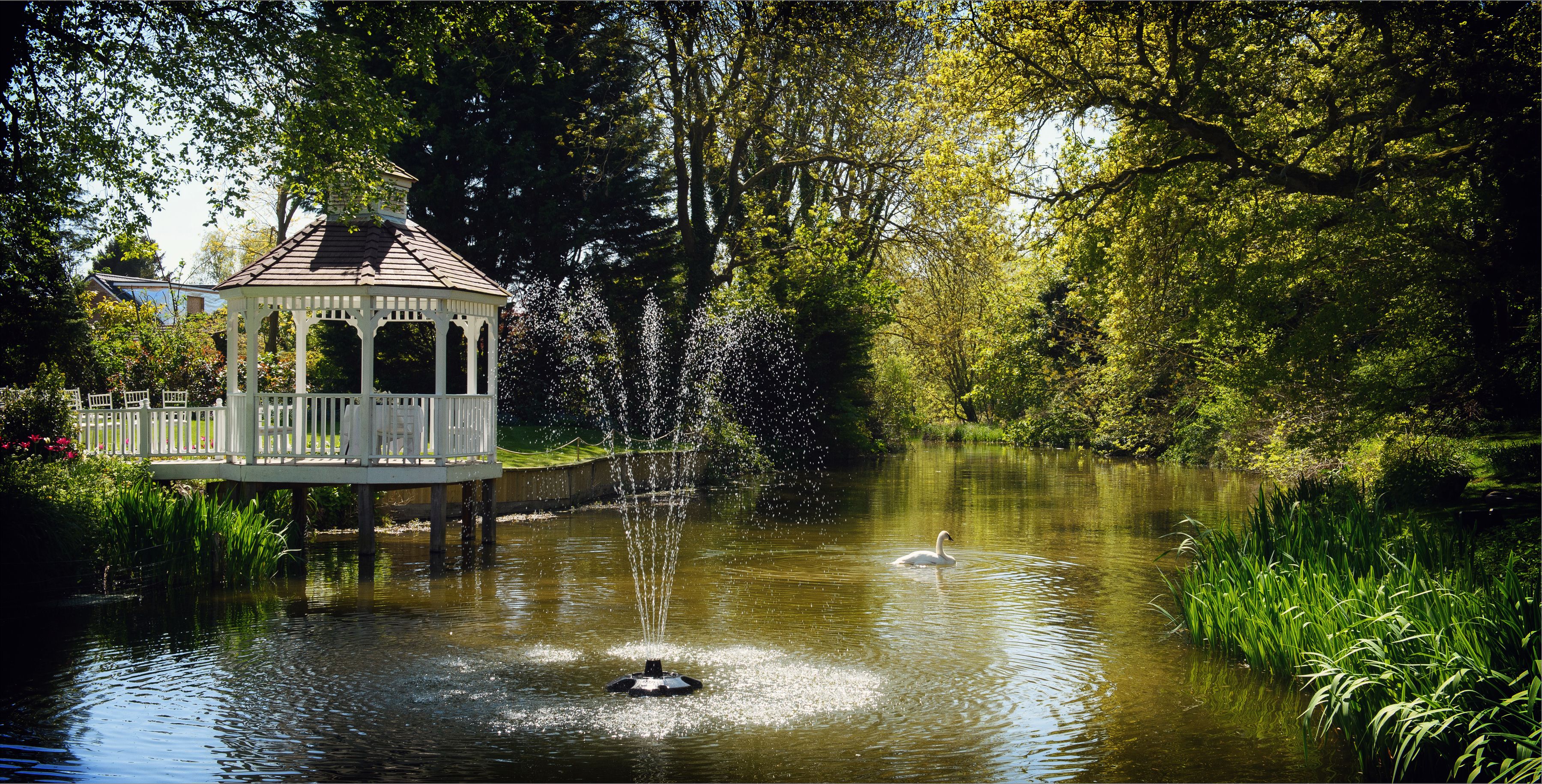 The white gazebo and fountain on the mill pond at Sheene Mill, framed by greenery