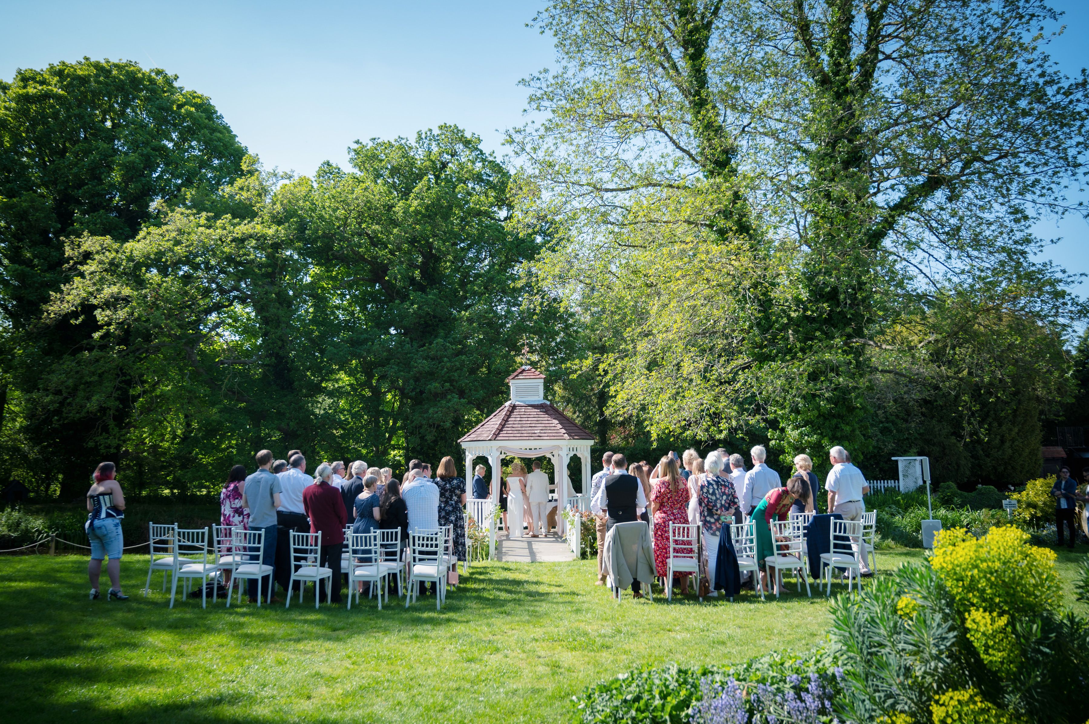 Guests gathered on the lawn for a summer wedding ceremony at the white gazebo in the gardens of Sheene Mill, Melbourn, Cambridgeshire