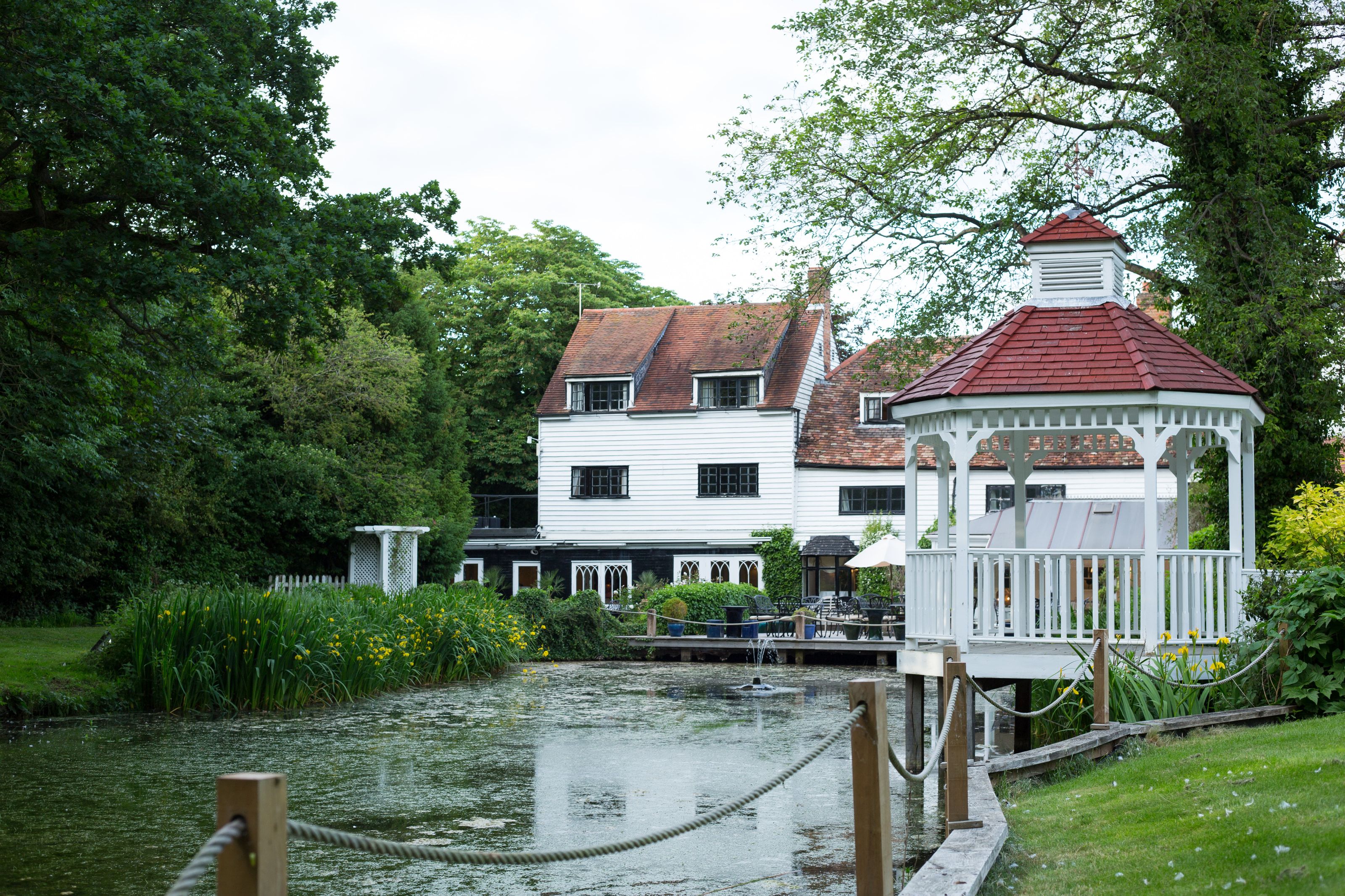 The white clapboard mill house at Sheene Mill seen across the mill pond, with the red roofed wedding gazebo and riverside gardens, in Melbourn, Cambridgeshire