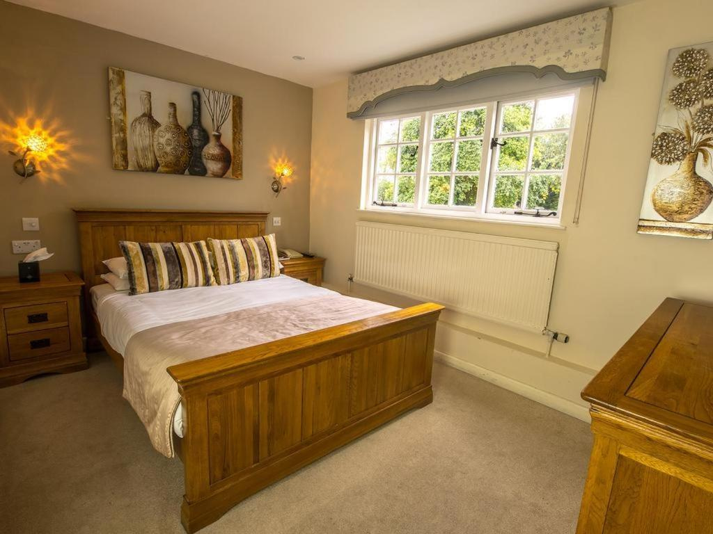 A boutique en-suite bedroom at Sheene Mill with an oak bed, warm wall lights and a window onto the garden, Melbourn, Cambridgeshire