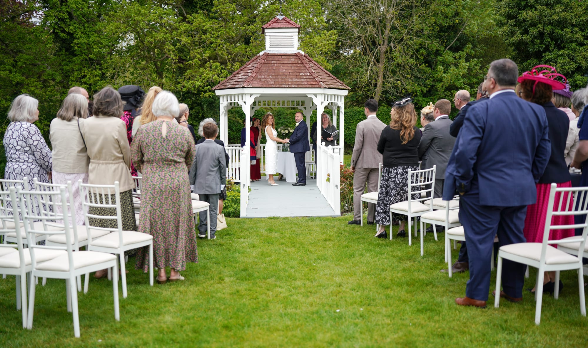 An outdoor wedding ceremony at the gazebo with seated guests in the gardens at Sheene Mill