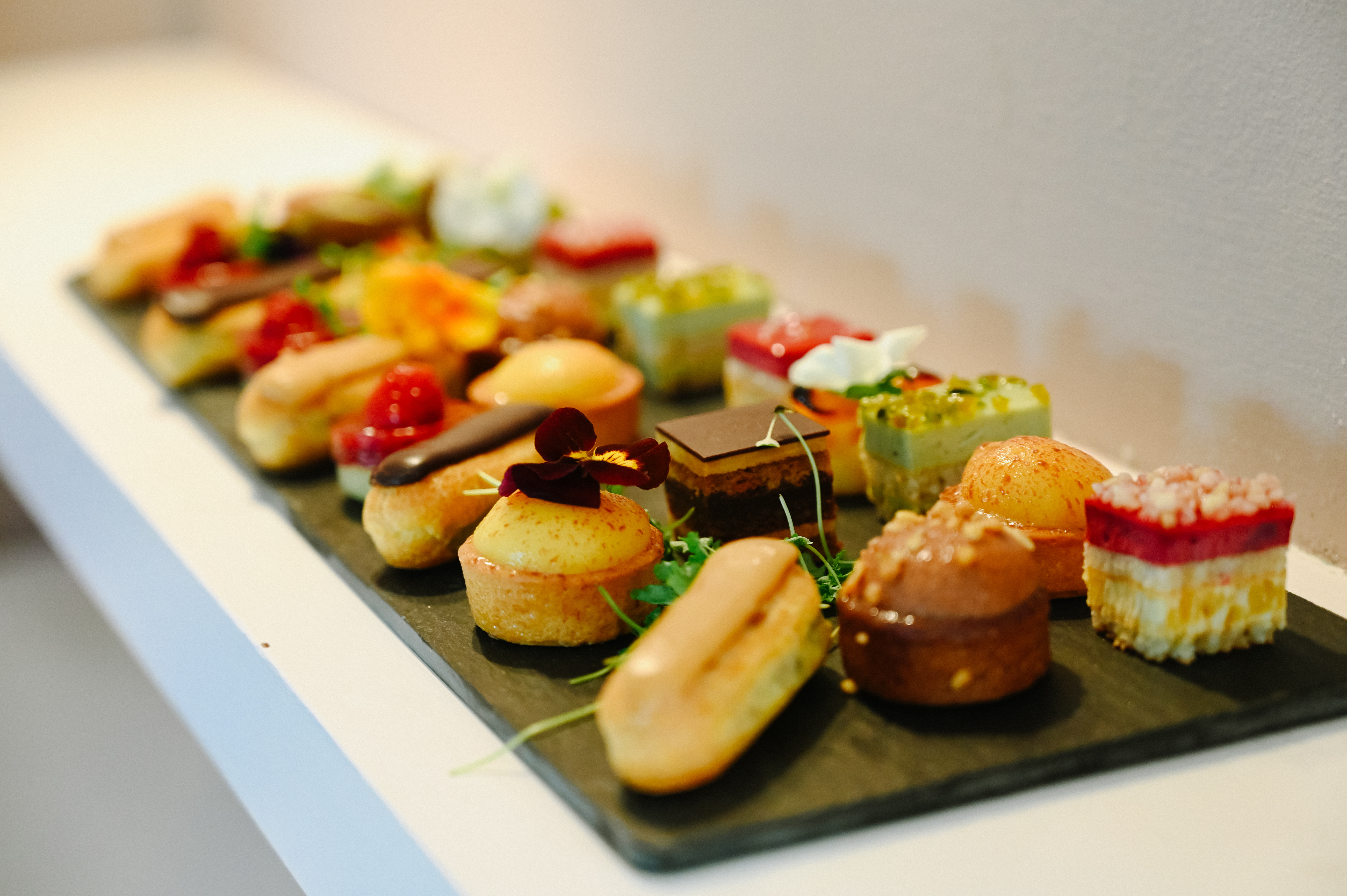 A slate of petits fours, from fruit tarts and eclairs to chocolate and pistachio slices, served at a private event at Sheene Mill, Cambridgeshire