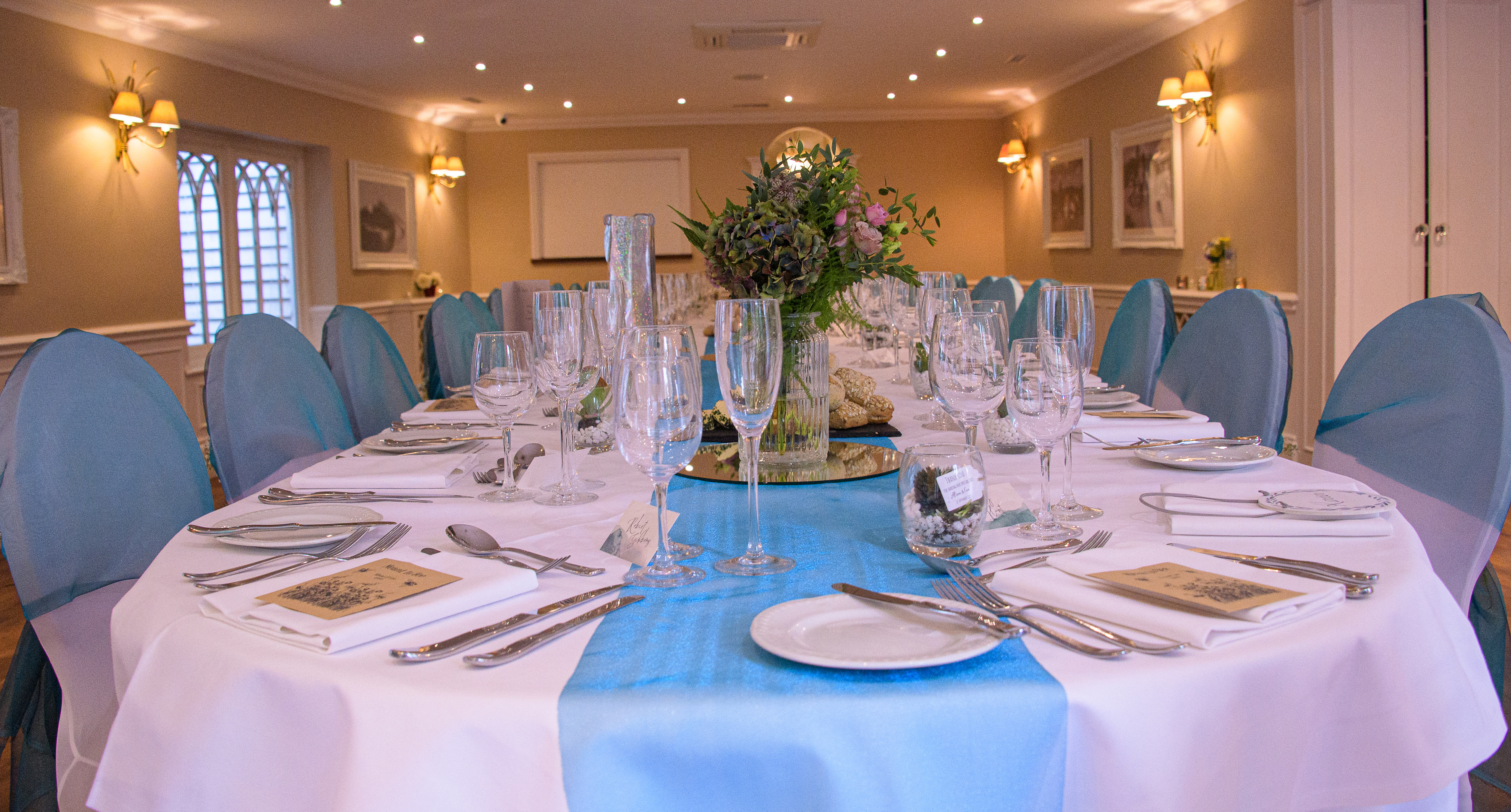 A long private dining table laid with white linen and a blue runner at Sheene Mill