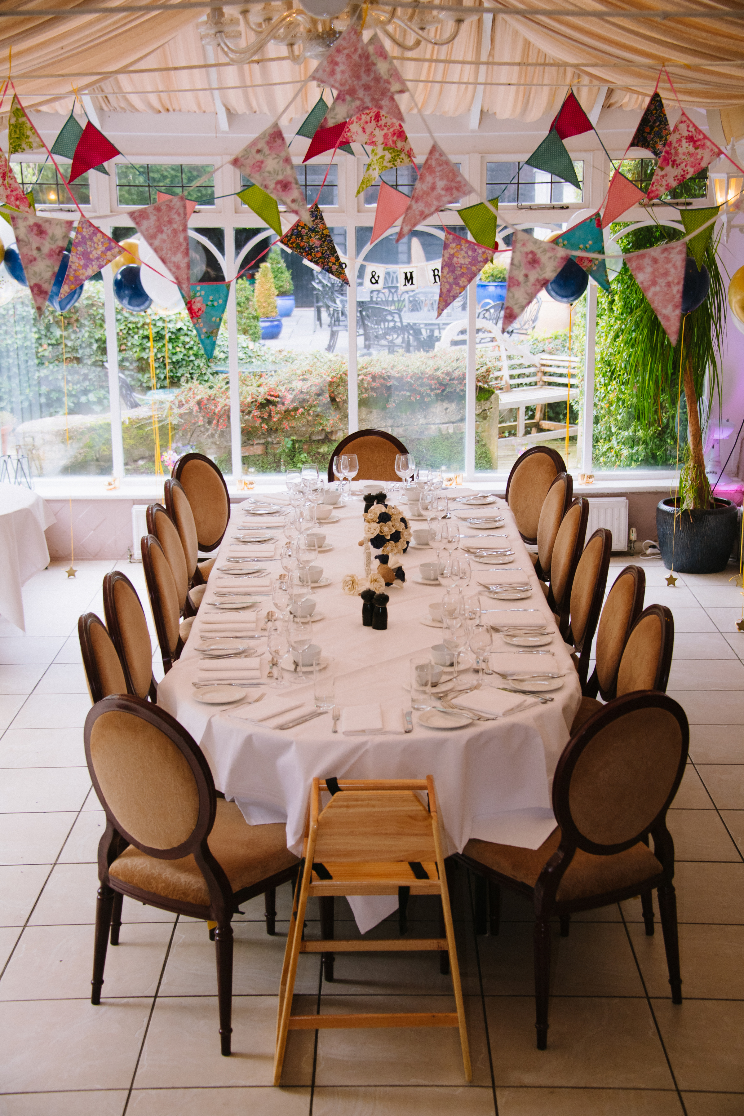 A long table laid for a private party in the conservatory at Sheene Mill, hung with floral bunting