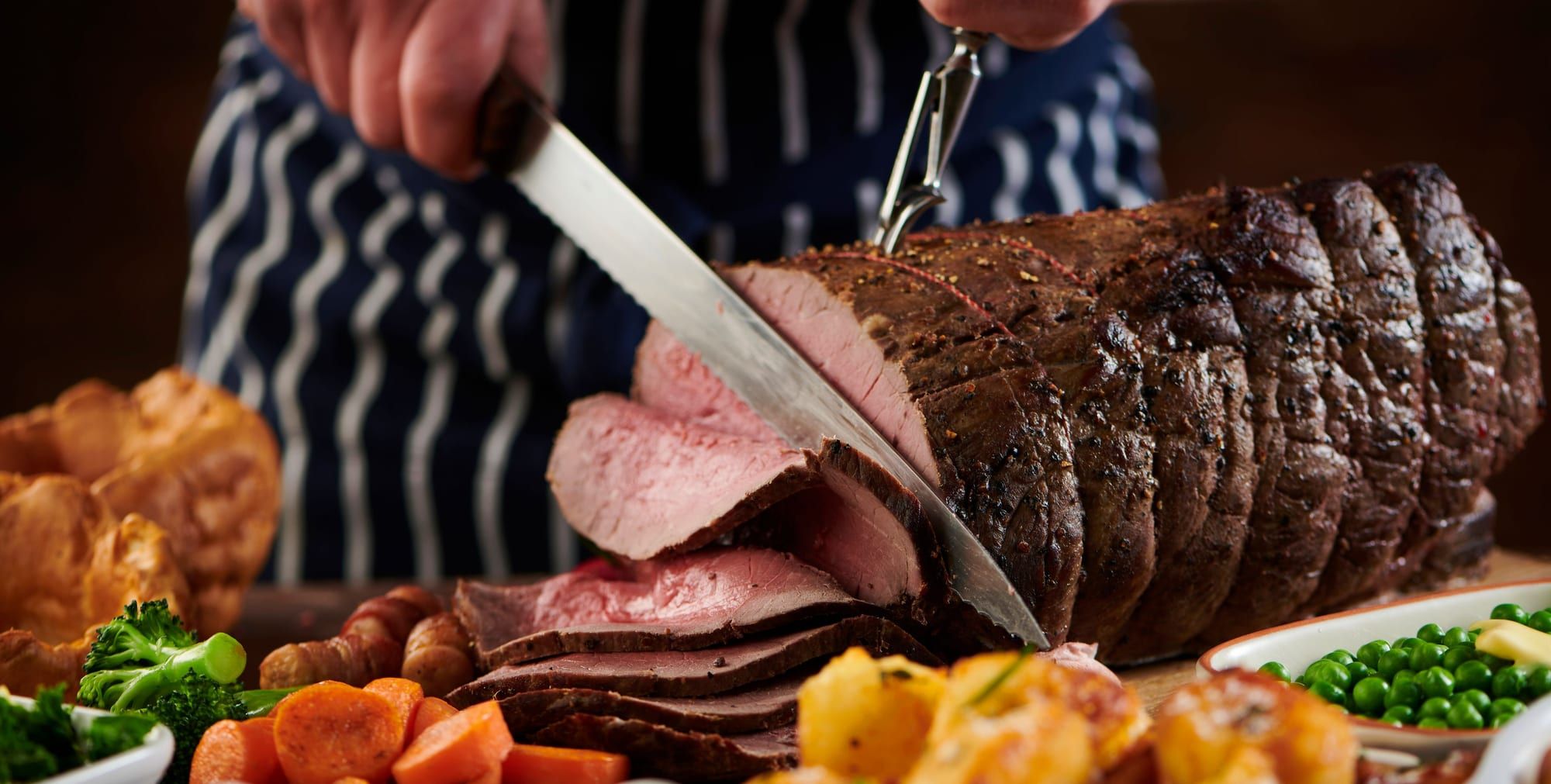 A chef carving a joint of rare roast beef with Yorkshire puddings, roast potatoes and vegetables for Sunday lunch at Sheene Mill, Melbourn, Cambridgeshire