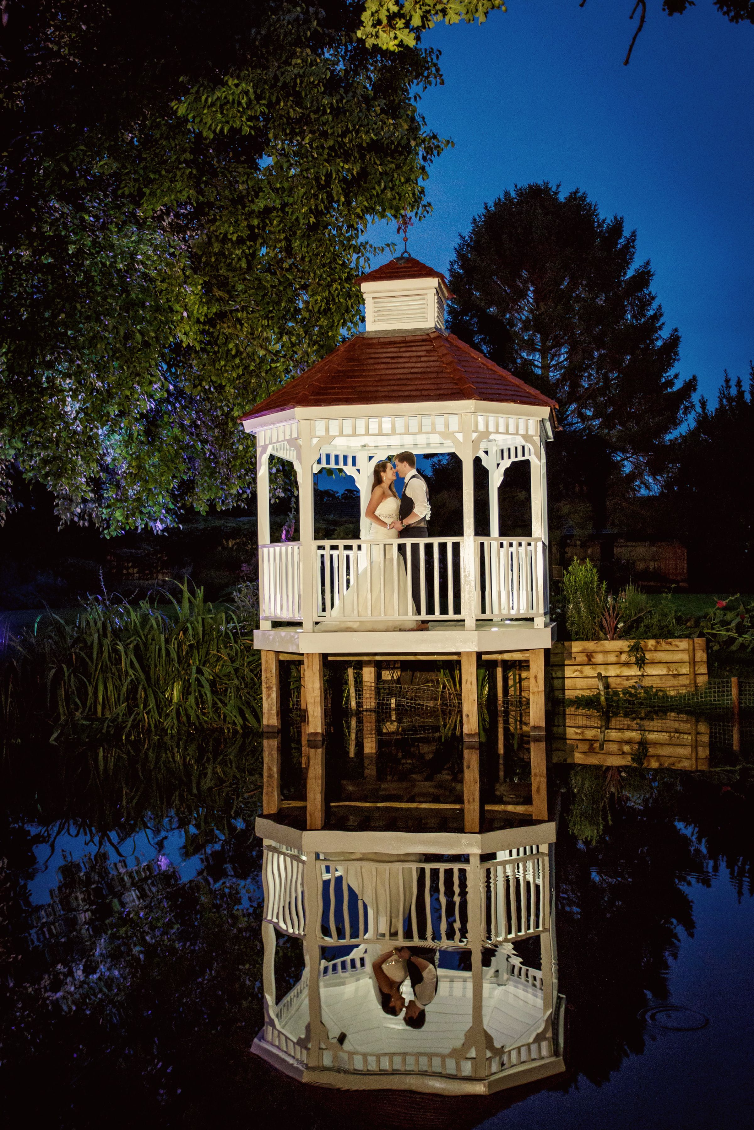 The mill house and gazebo at Sheene Mill lit at dusk, reflected in the millpond