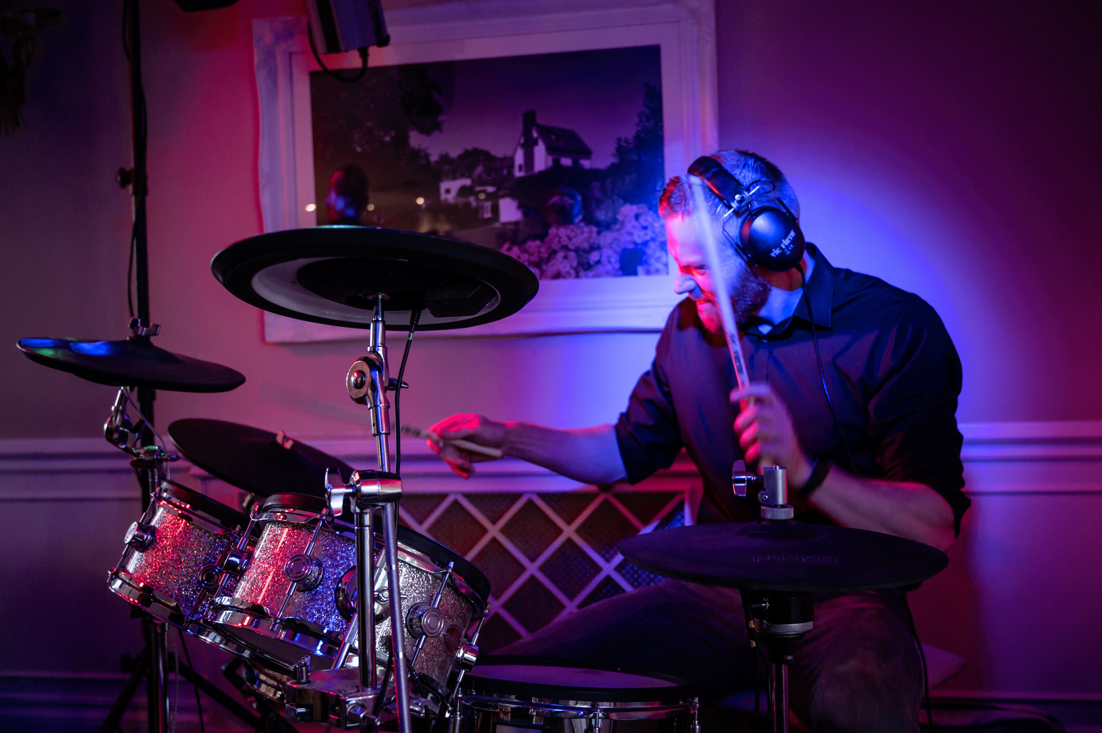The wedding band drummer playing under purple lights during the evening reception at Sheene Mill