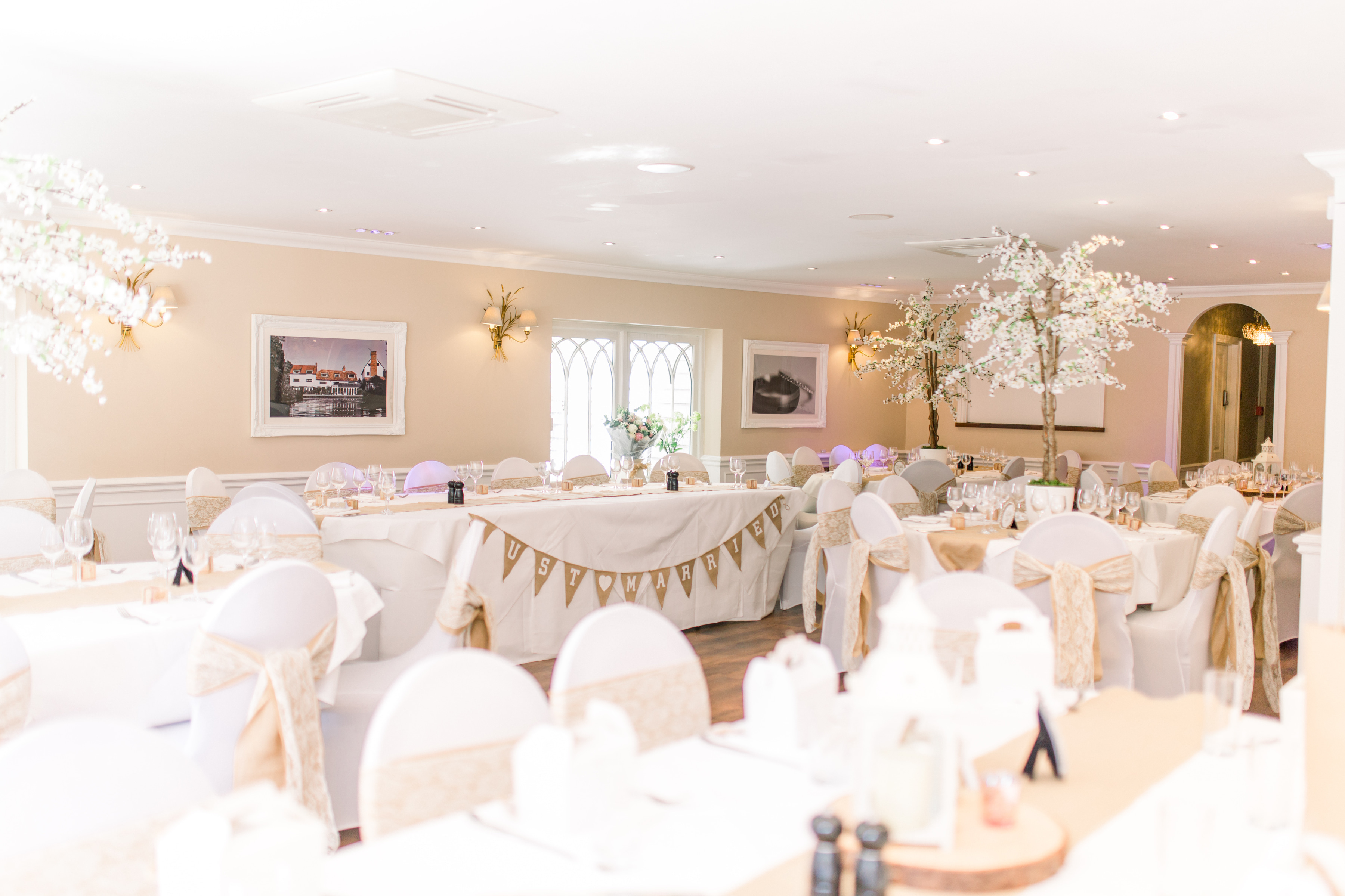 The wedding breakfast room at Sheene Mill set with dressed chairs, bunting and pale blossom