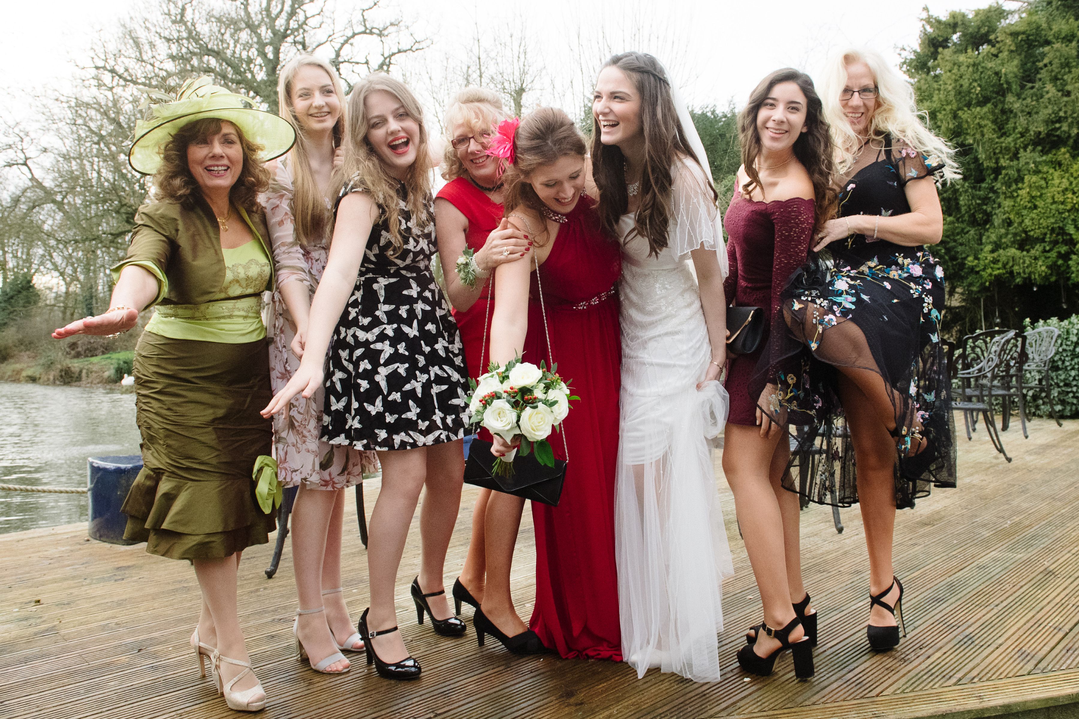 A bride laughing with a group of wedding guests on the riverside decking at Sheene Mill