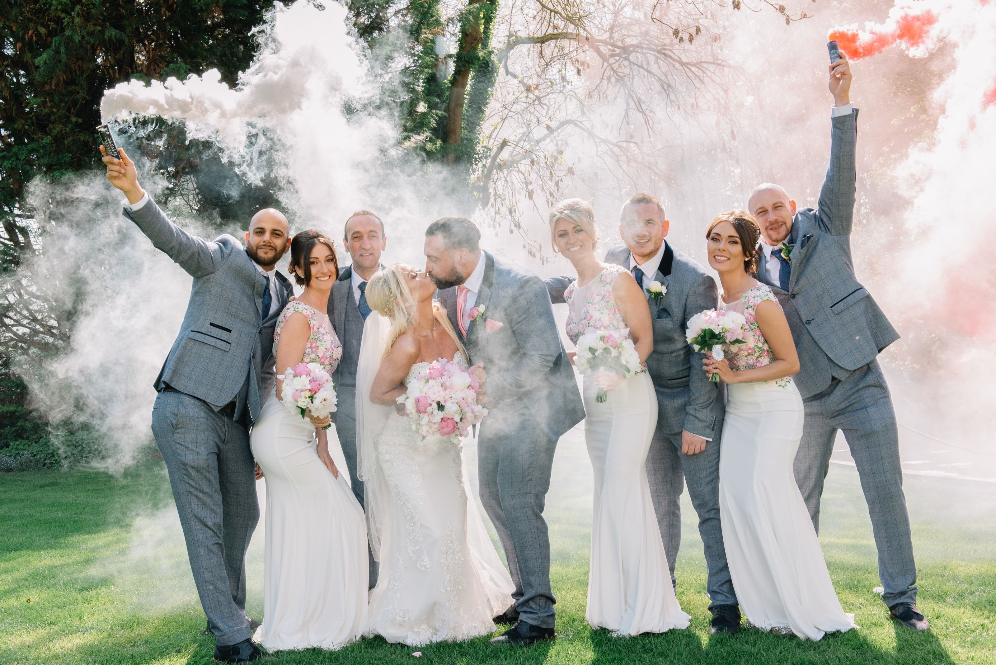 A wedding party celebrating with smoke flares on the lawn as the bride and groom kiss at Sheene Mill, Cambridgeshire