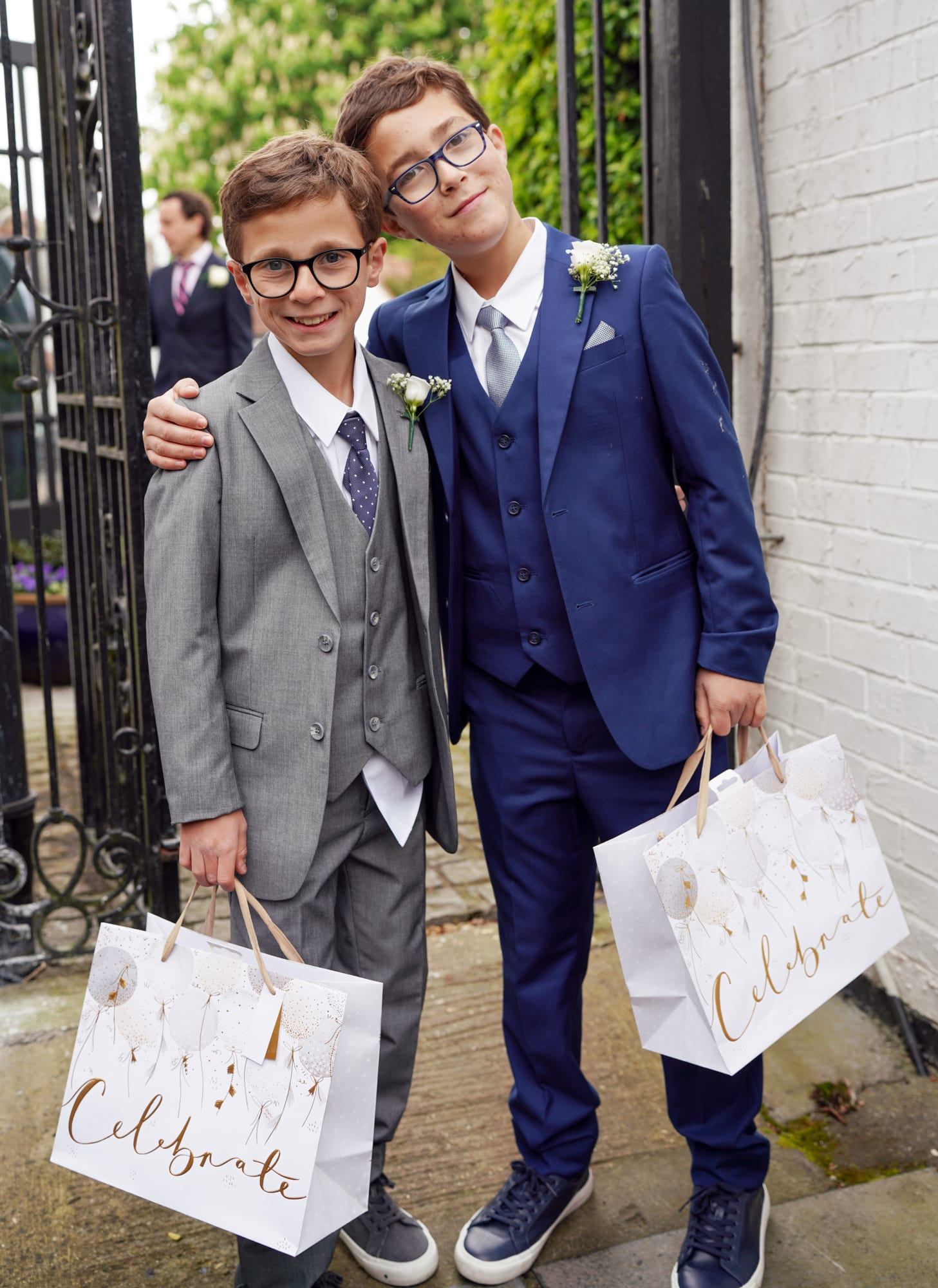 Two young wedding guests in suits carrying celebration gift bags at Sheene Mill